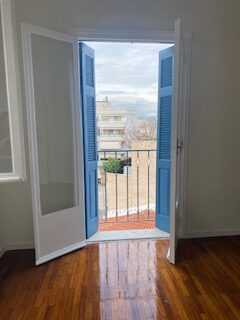 Sunlit room with parquet floor opening onto a balcony with blue shutters
